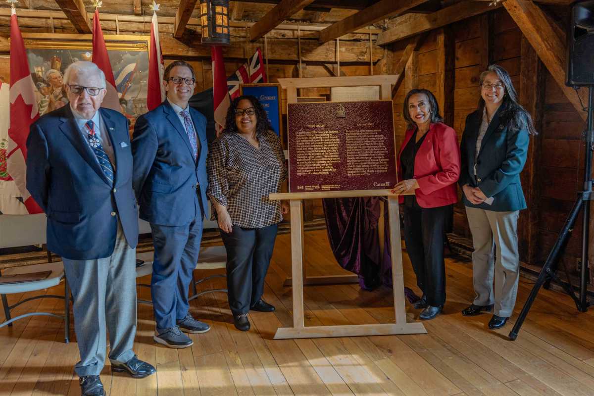 A group of people standing up beside a commemorative bronze plaque on a wooden stand