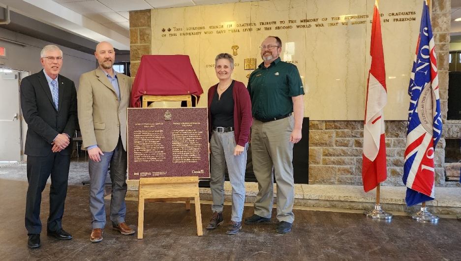 Group of people standing with a bronze commemorative plaque inside a building