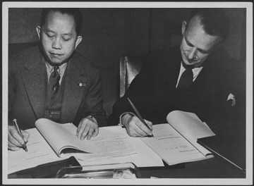 Deux hommes signant des documents à un bureau. 