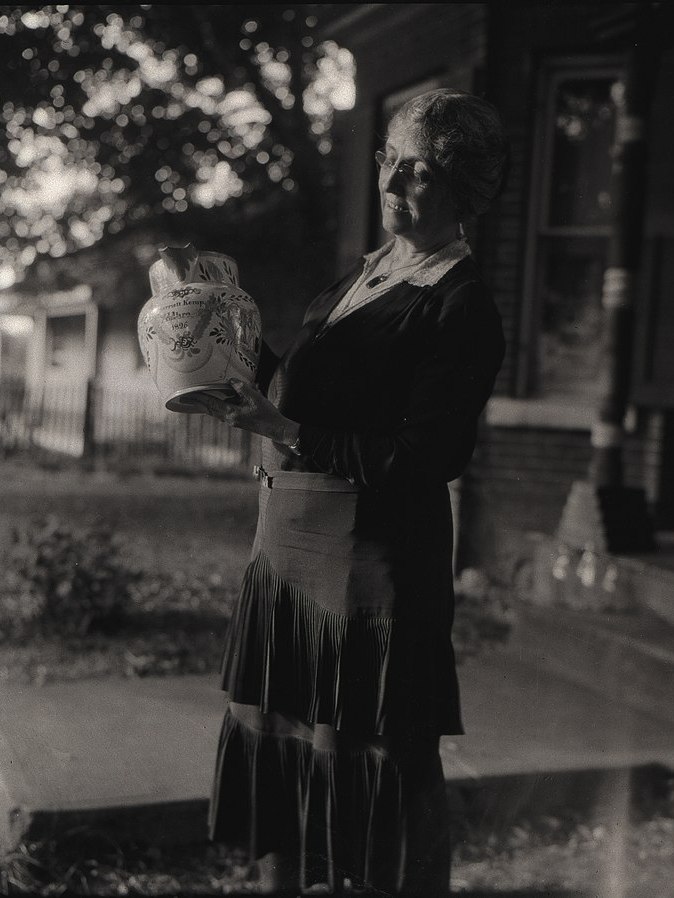 Photo en noir et blanc d'une personne debout tenant un vase dans ses mains, dans un environement extérieur