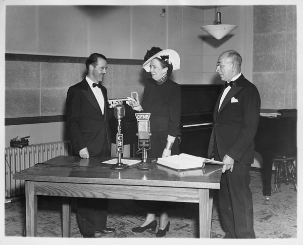 Black and white photo of three persons standing in front of a desk