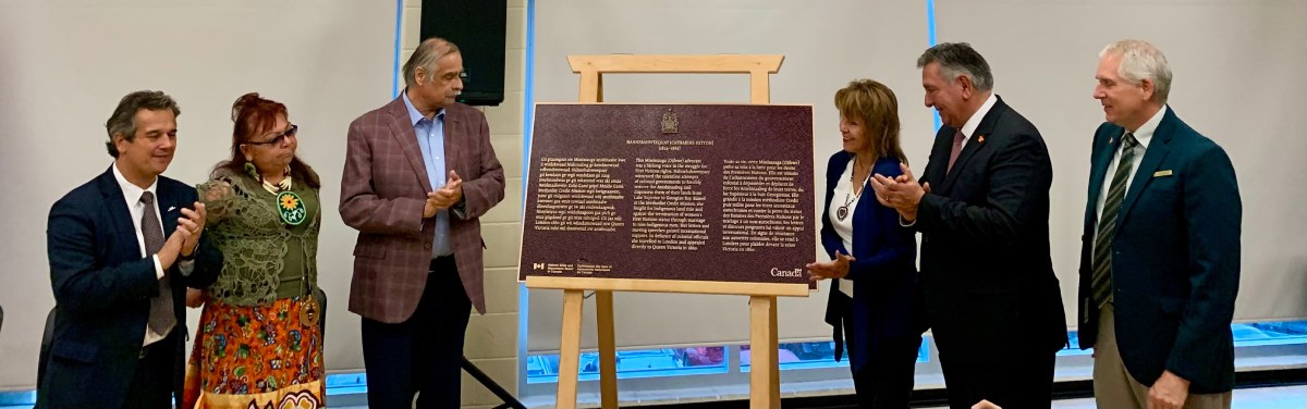 Un groupe de personnes sont bebout près d'une plaque commémorative installée sur un chevalet