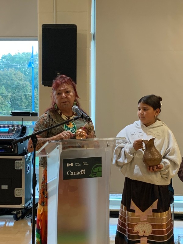 Une femme devant un lutrin adresse un discours lors d'un événement officiel et se tient près d'elle une jeune fille