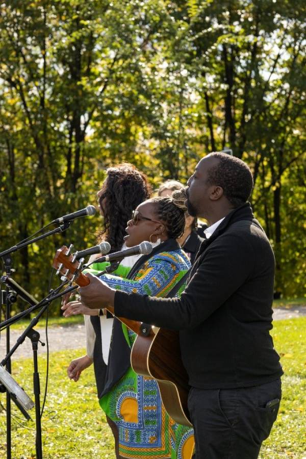 Three people sing and play music in an outdoor setting