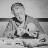 A woman handles bones, sitting at a desk