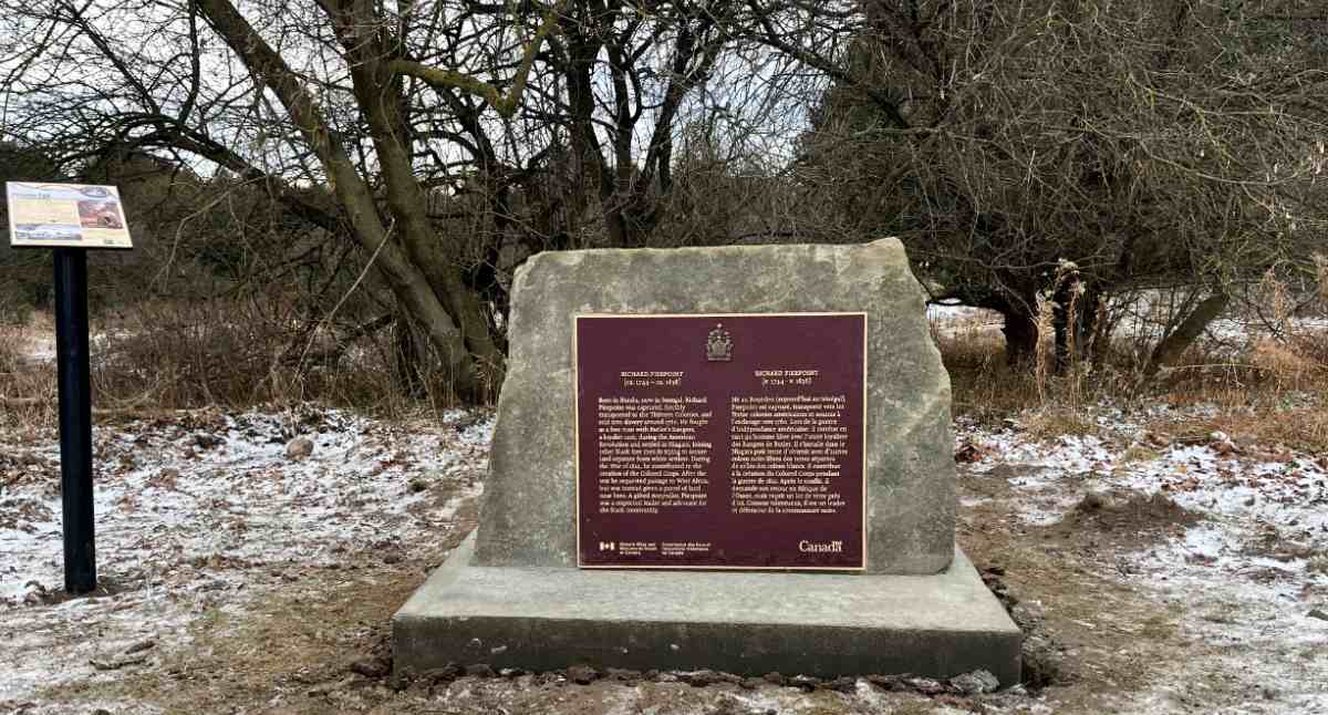A bronze commemorative plaque on a concrete mount in a wintery setting