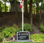 Un pierre de sépulture entourée d'arbres et un drapeau du Canada