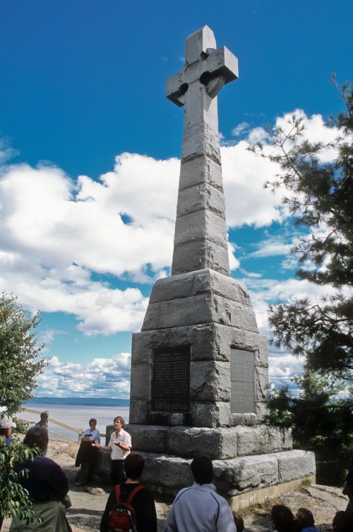 Commemorative cross-shaped monument with blue sky and people walking around it
