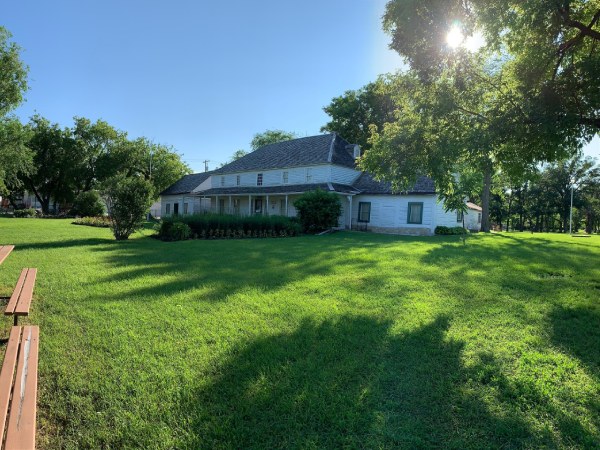 Vue d'une grande maison blanche et verte entourée d'arbres et d'herbe verdoyante
