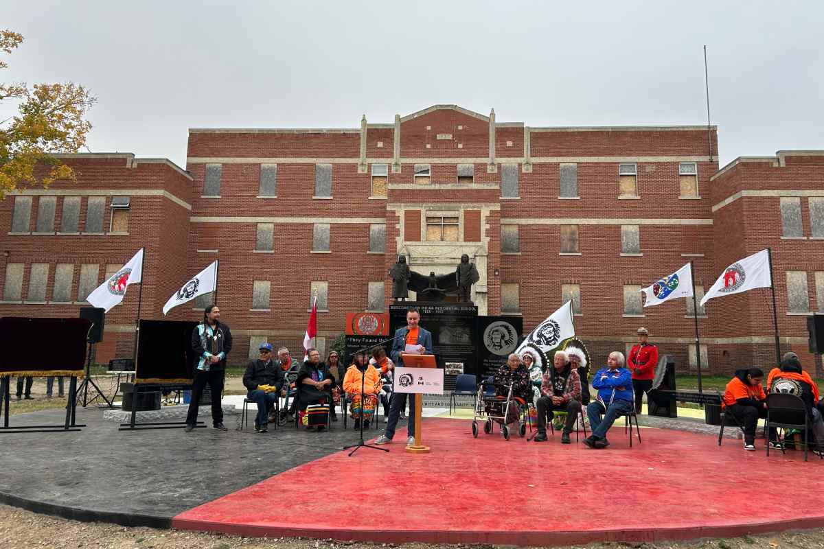 Group of people standing and sitting on a stage in front of a large building