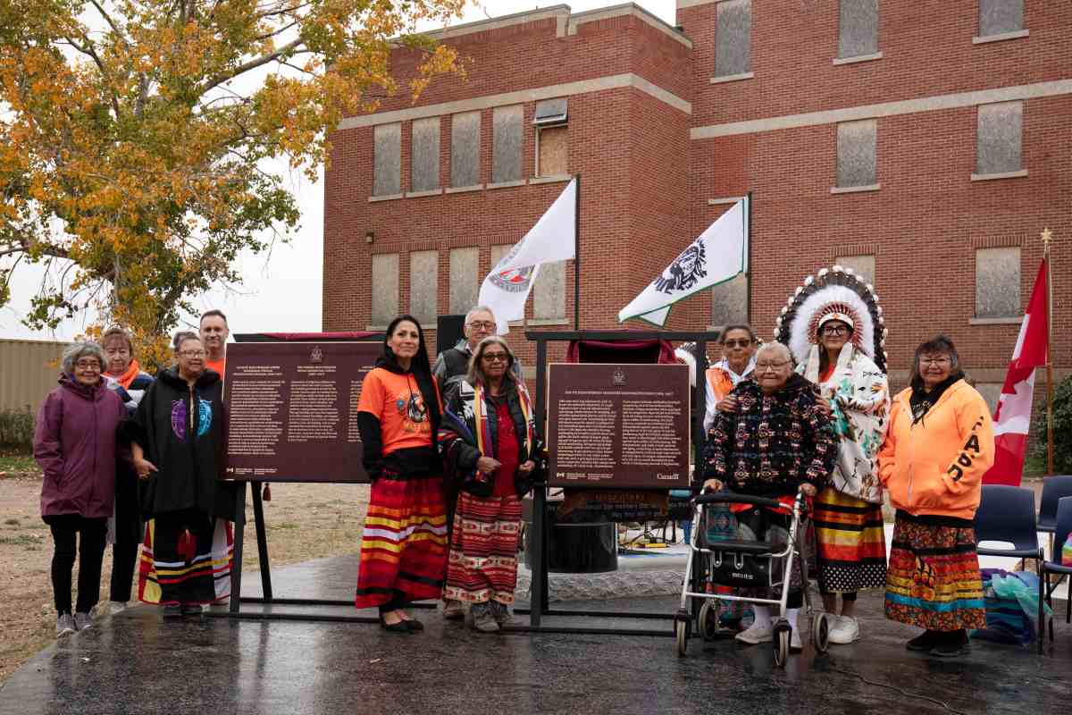 Group of people standing and sitting on a stage in front of a large building, unveiling commemorative plaques