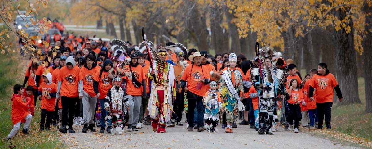 Group of people dressed in color orange walks down a path surrounded by trees