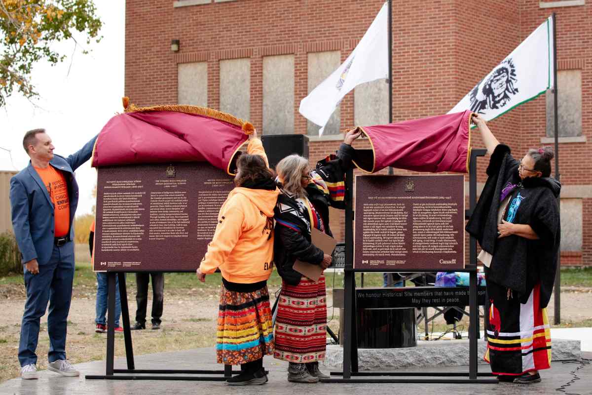Group of people standing and unveiling commemorative plaques in front of a large building