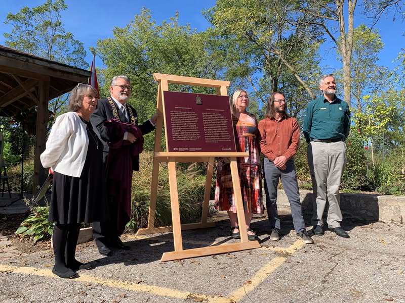A group of people are standing near a commemorative plaque held on an easel