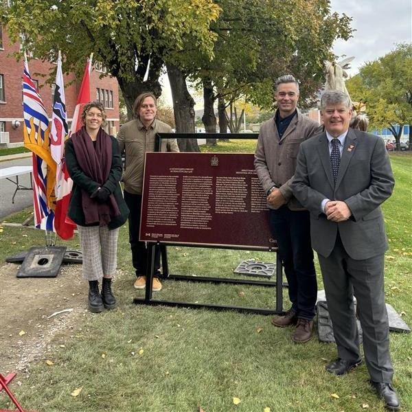 A groupe of people stand beside a commemorative plaque for Kamloops Residential School
