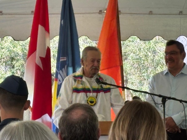 A man speaks into a microphone in front of a crowd with flags behind him