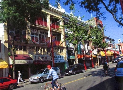 A street in a chinatown, buildings, cars, pedestrians and people biking