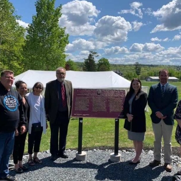Un groupe de personnes debout près d'une plaque commémorative en bronze dans un décor extérieur