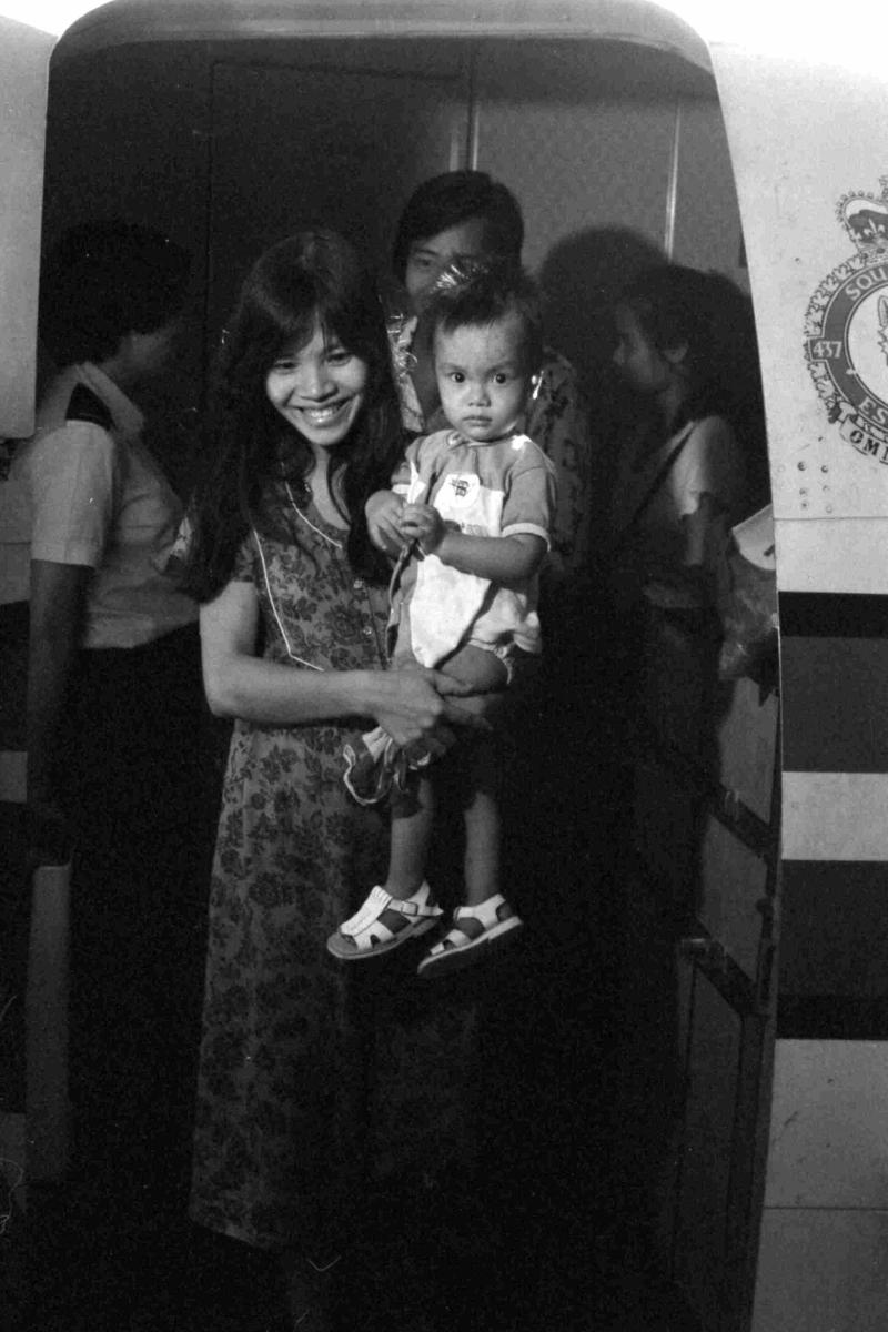 Black and white photo of an adult holding a child and exiting an airplane