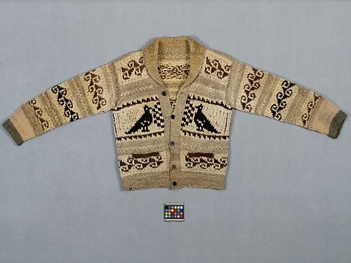 A Cowichan sweater with waves and birds motifs is displayed on a grey surface