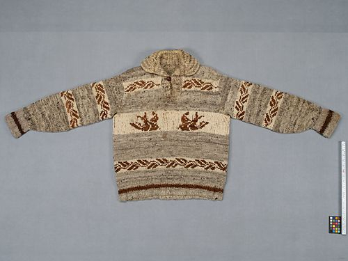 A Cowichan sweater showcased on a grey surface shows patterns of birds