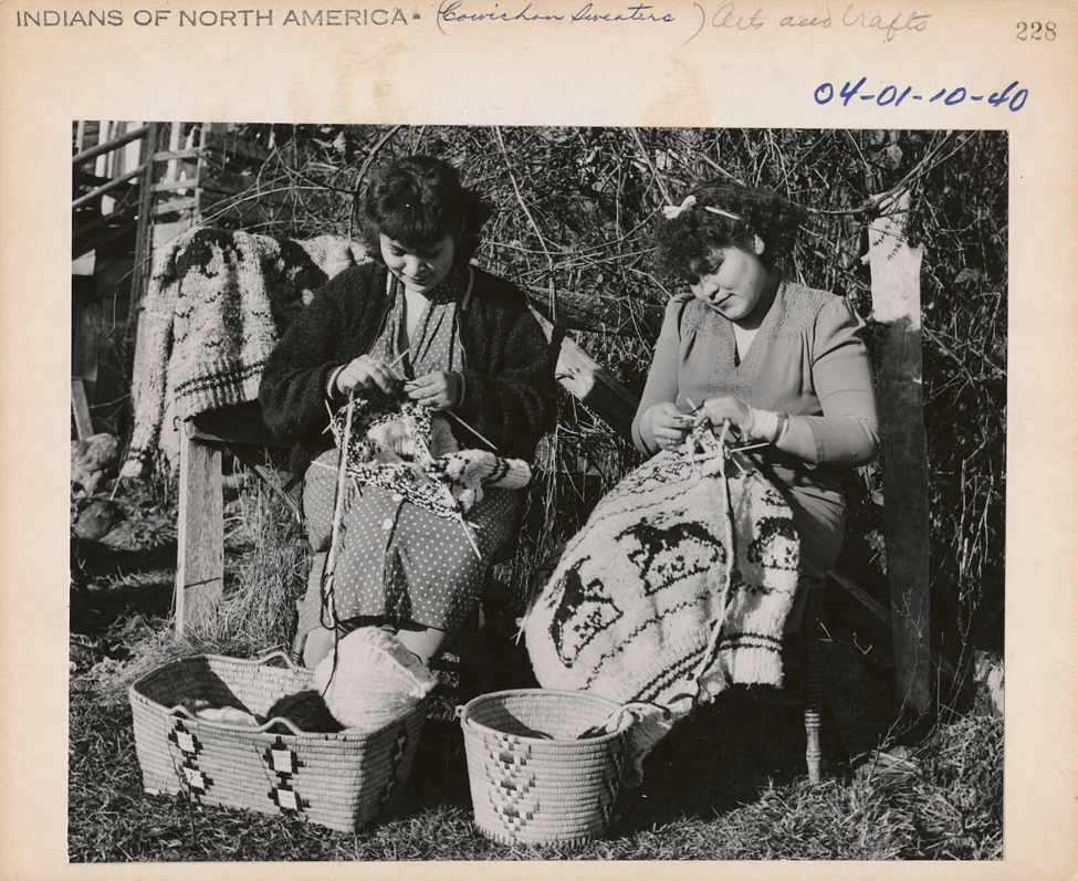 Two women are knitting with wool, sitting with large baskets in front of them