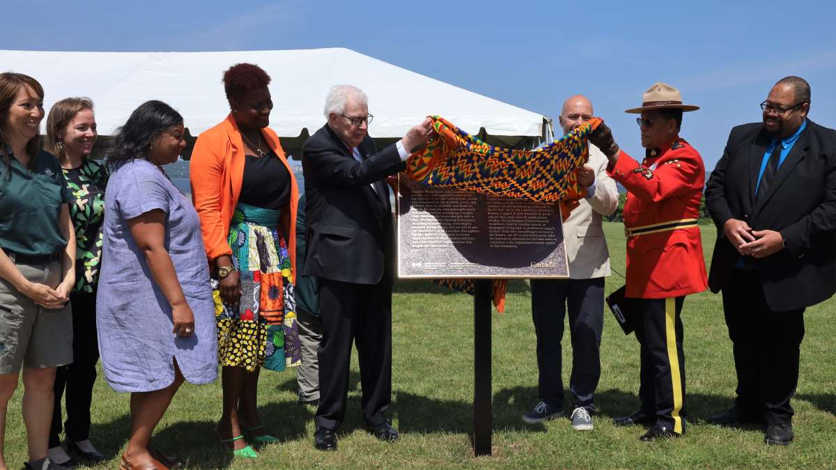 Groupe de personnes à l'extérieur, dévoilant une plaque en bronze et ciel bleu