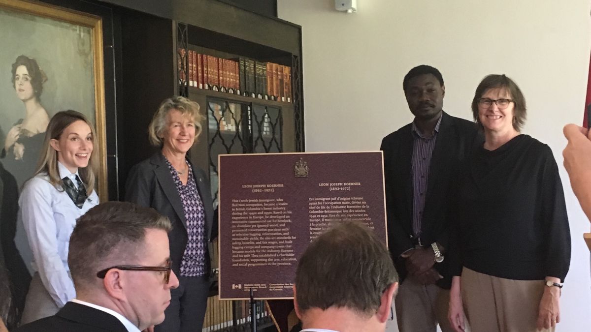 A group of people stand near a commemorative plaque in an indoor setting