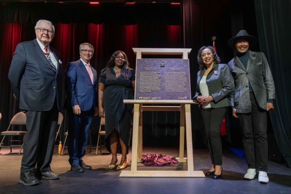 Un groupe de personnes debout près d'une plaque commémorative en bronze