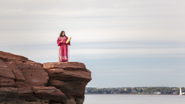 A Mi'kmaq woman plays a drum on a cliff overlooking the mouth of the Hillsborough River.