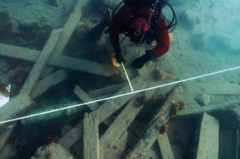 Diver lays out a quadrant of white lines over top of debris scattered on the ocean floor.