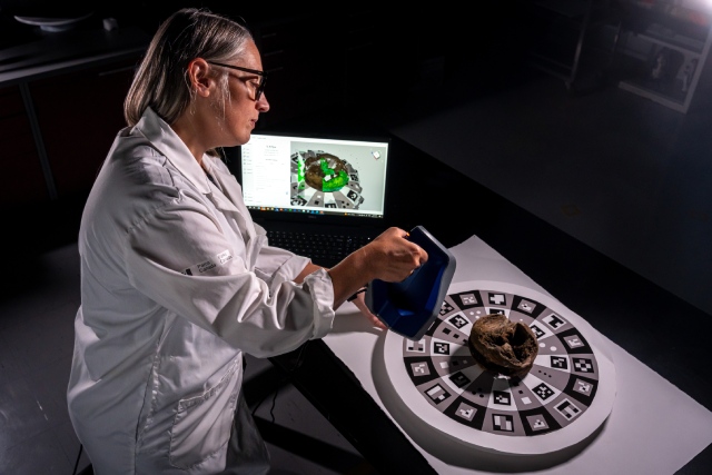 A person scans an artifact with a handheld scanner in a dimly lit laboratory, the image is displayed on a computer screen