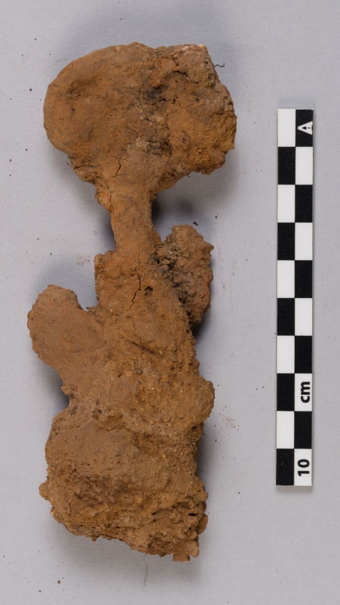 A rusted key artifact ont a grey flat surface beside a measuring tape