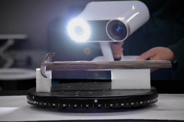 A person holds a portable scanner that projects a bright white light on a historical axe