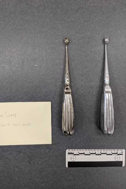 Deux petites cuillères médicales en métal présentées côte à côte, dont l'une est une reproduction et l'autre l'original. Les deux objets se ressemblent en forme, en couleur et en texture.