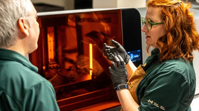 Deux personnes en uniforme se tiennent à côté d'une imprimante 3D