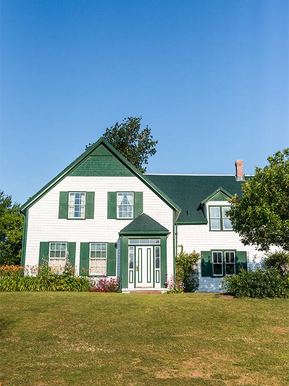 The front of a white historic building with green trim is seen from its front lawn.