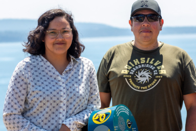 Tiffany Joseph et Ish Peters se tiennent devant un appareil audio avec la mer des Salish en arrière-plan.