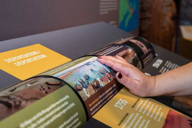 La main d'un visiteur interagit avec une roue qui comporte du texte, faisant partie de l'exposition.