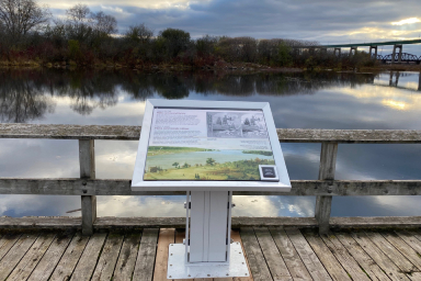 Un vue sur l'eau et un panneau d'interprétation extérieur racontant l'histoire de la pêche commerciale des Métis.