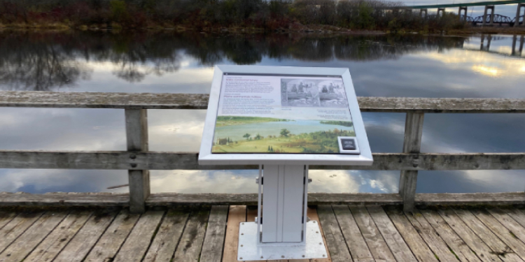 Un vue sur l'eau et un panneau d'interprétation extérieur racontant l'histoire de la pêche commerciale des Métis.