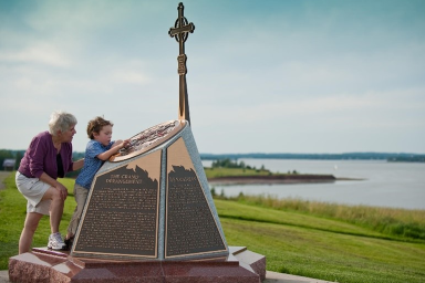 Une femme et un jeune garçon debout devant un monument historique. Le garçon a la main sur le dessus et la regarde attentivement.