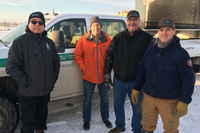 Un groupe de quatre personnes sourit en hiver en avant d’un véhicule de Parcs Canada et d’une remorque.