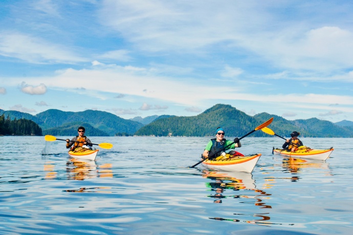 Three kayakers paddle in glassy blue waters.