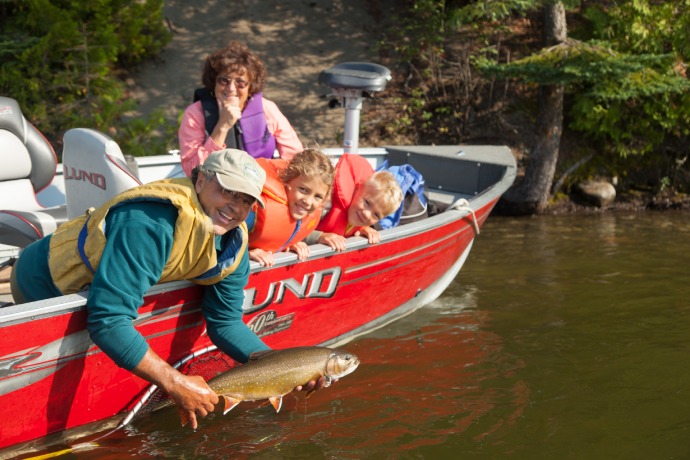 Deux parents et deux enfants sourient à bord d’un petit bateau. Le père tient un poisson hors de l’eau.