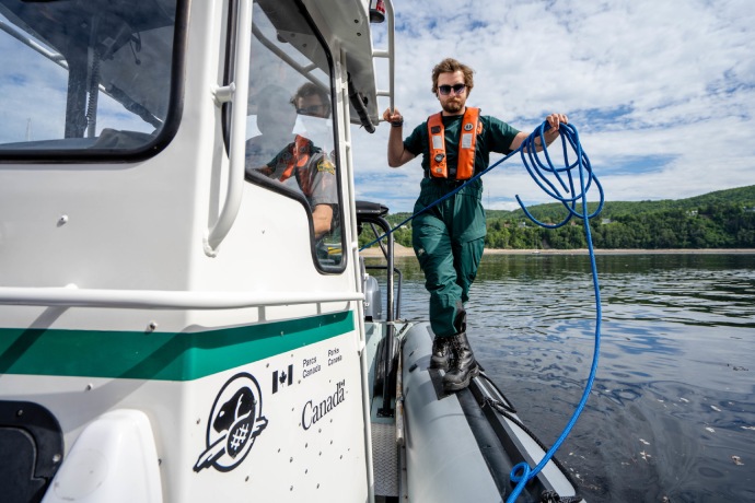 Un employé de Parcs Canada marche, sur le bord d’un bateau sur l’eau, en tenant une corde.