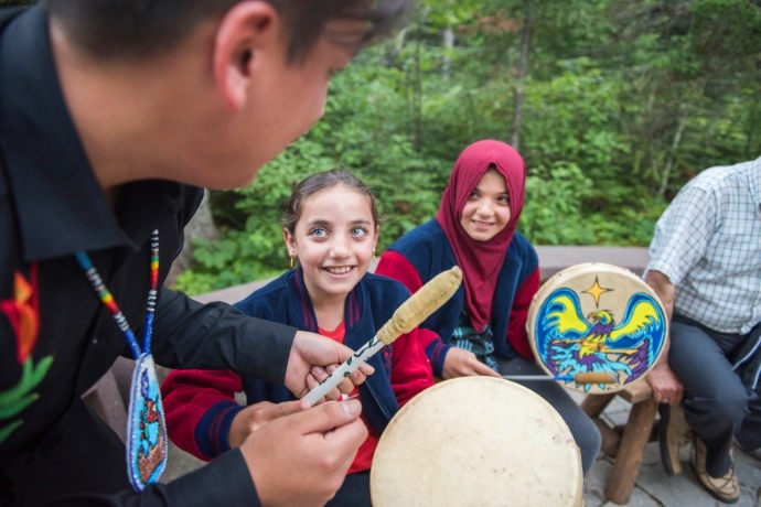 Two children are being taught how to play the hand-drum by a skilled teacher.