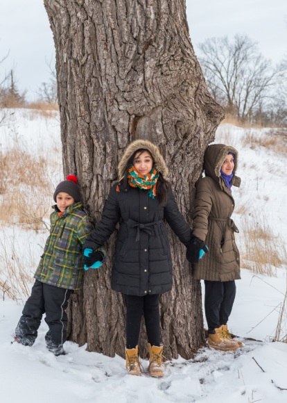 Three youth lean on a large tree in the wintertime while holding hands.