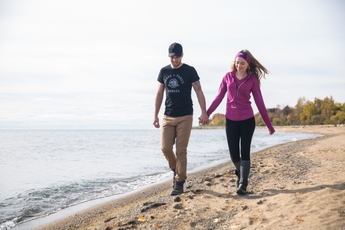 Two people hold hands walking along the shores of a beach.