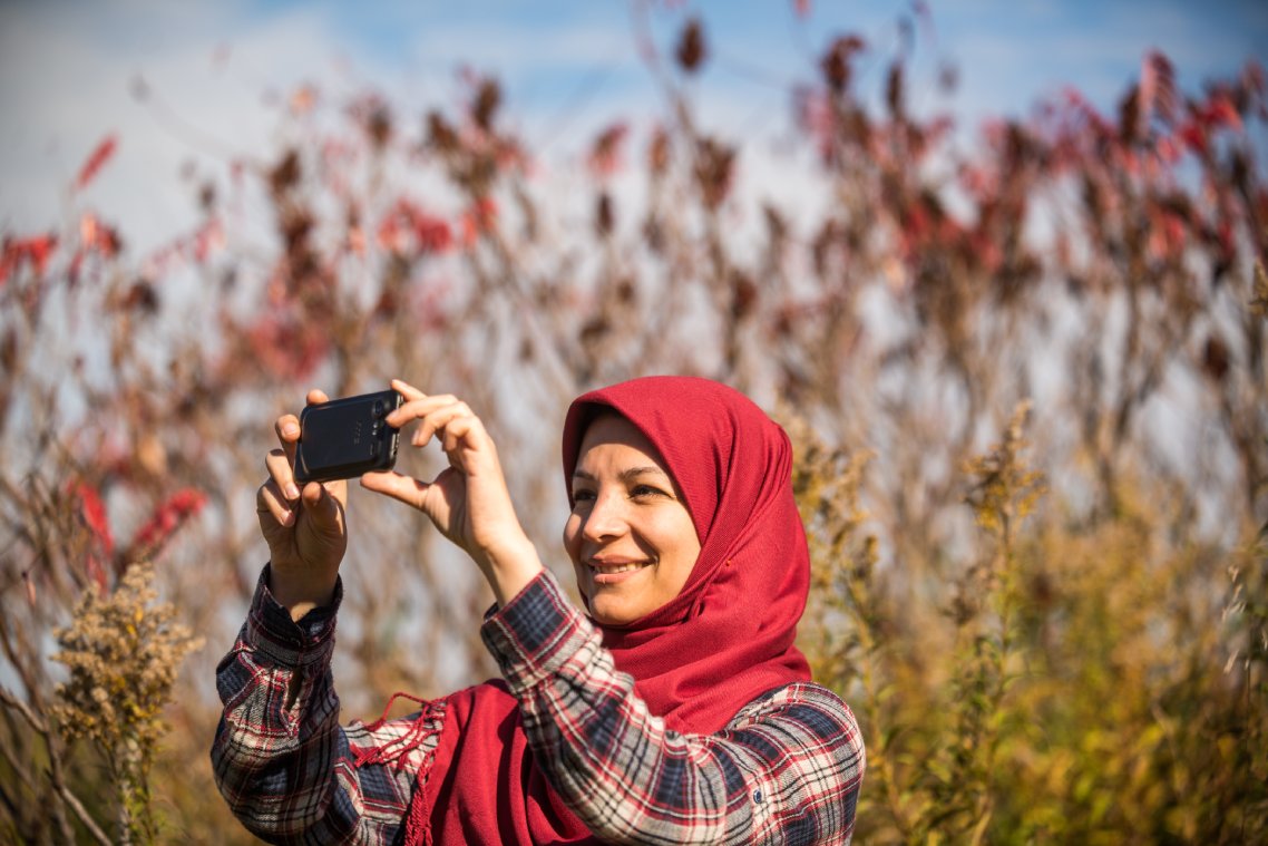 A person smiles while taking a photo among tall grasses.